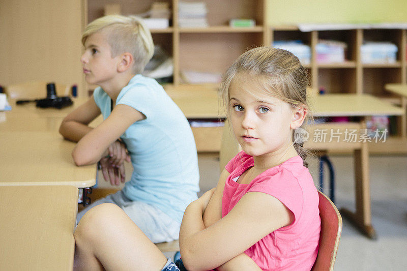 肖像:可爱的金发女学生坐在教室里，双臂交叉