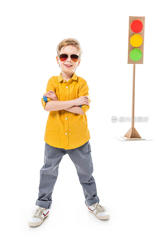 微笑的男孩戴着太阳镜，双臂交叉摆姿势，孤立在白色与纸板红绿灯，孤立在白色