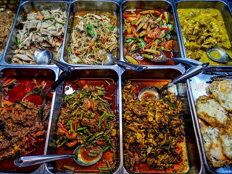 典型的泰国街头小吃咖喱和汤装在金属托盘里，在泰国的街头小吃摊上等待人们用勺子舀到蒸白米饭。