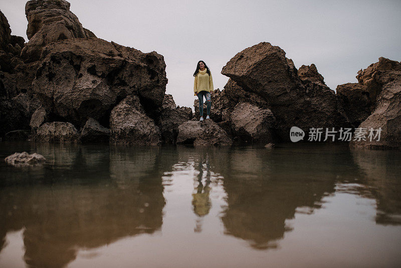 一个年轻女子在海滩的岩石和她在水中的倒影