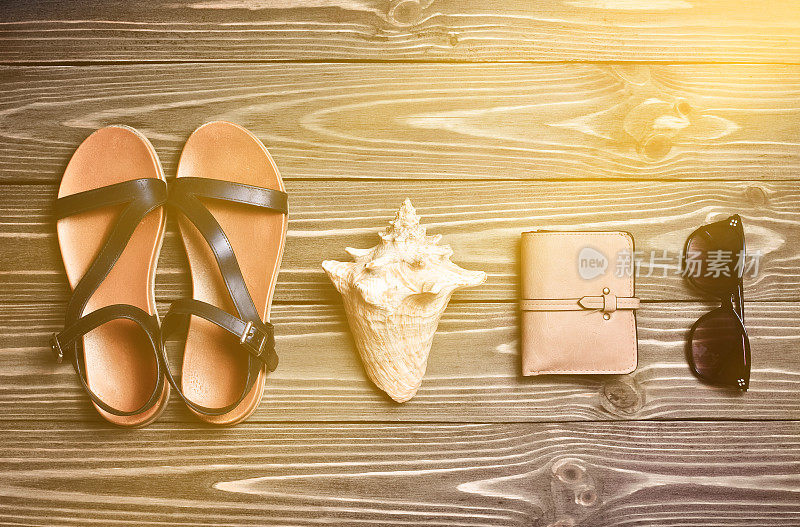 旅行的概念。凉鞋，贝壳，钱包，太阳镜在木制的表面上。前视图。平的。