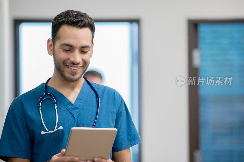 年轻的西班牙裔医生微笑着在数字平板电脑上阅读电子病历