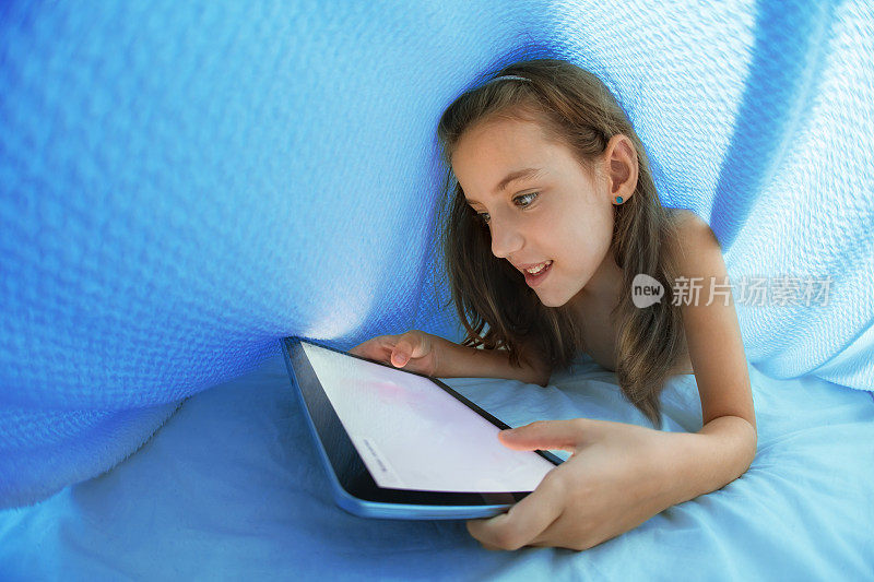 小女孩睡在羽绒被下使用她的电子平板电脑