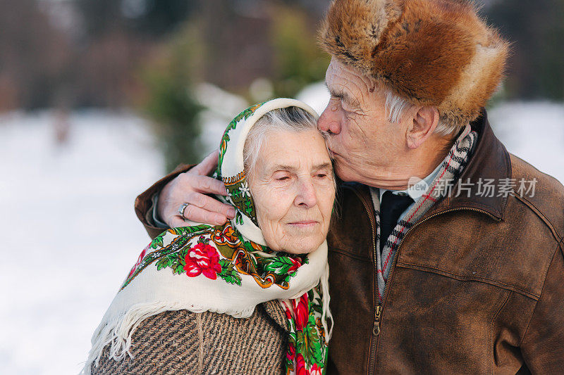 老年夫妇的肖像。老人亲吻他的妻子在重量。冬天的时候，一对老夫妇在公园里散步。幸福的家庭。金婚