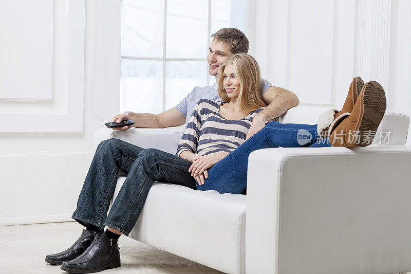 一对年轻的白人夫妇坐在沙发上拿着遥控器