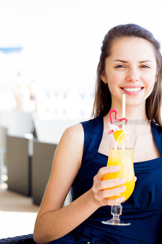 年轻微笑的女人与橙汁摆姿势在咖啡馆的户外