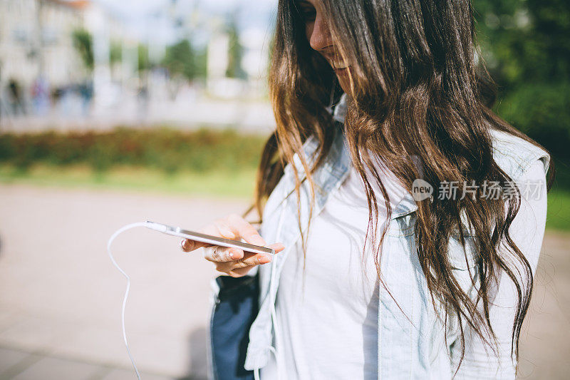 年轻的黑发女子正在用智能手机听音乐