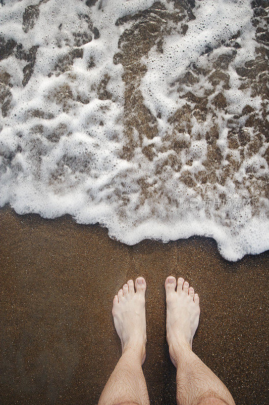 双脚站在沙滩上，海浪拍打着海岸