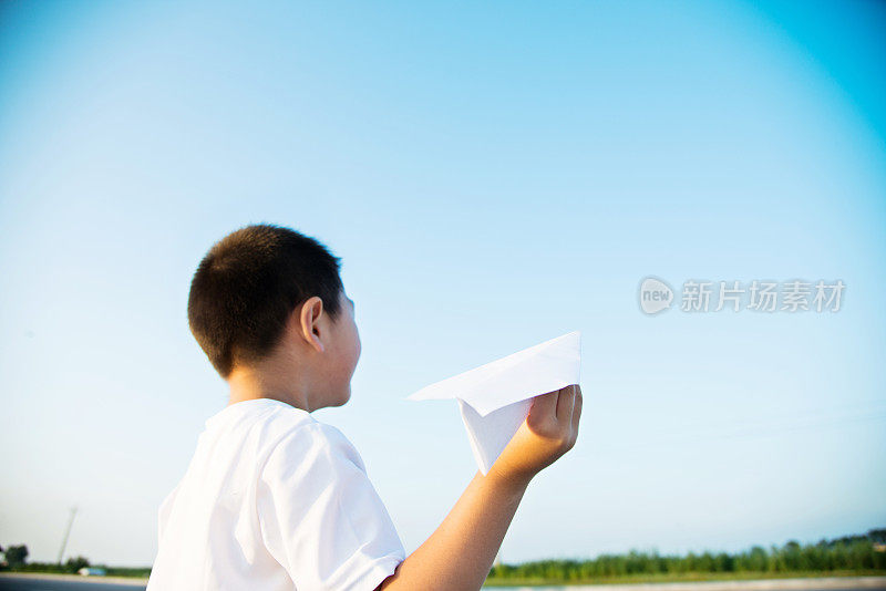 男孩手拿着纸飞机望着天空