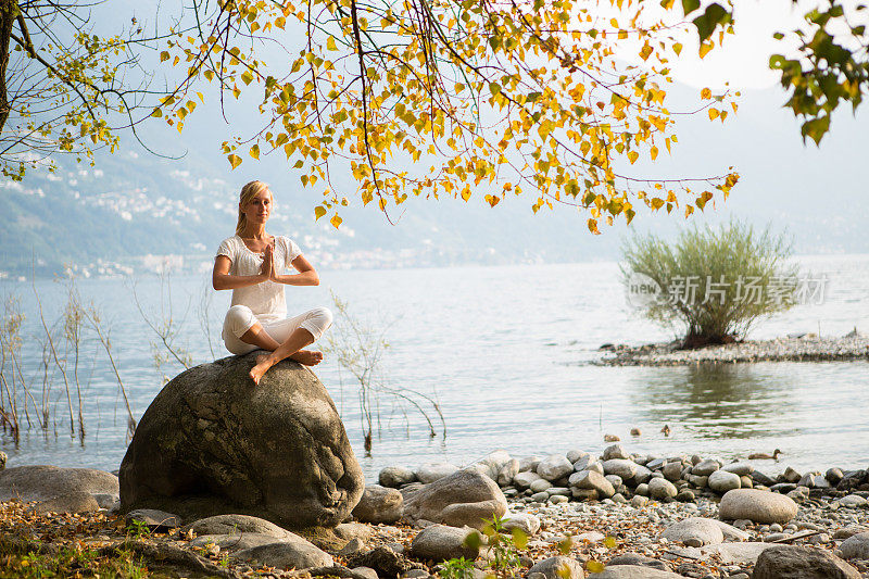 一个女人在湖边的岩石上练习瑜伽