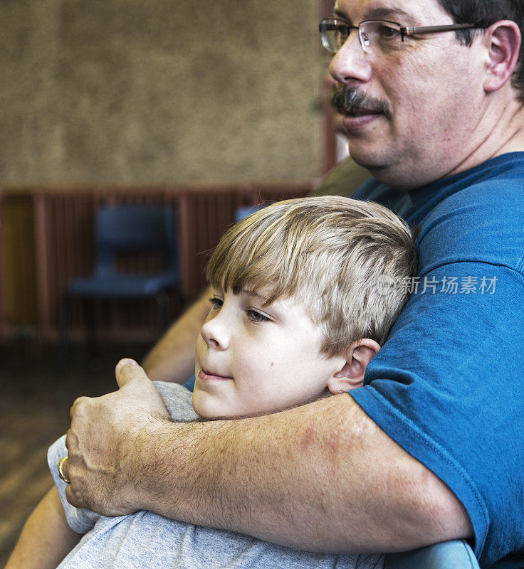 父亲坐在教室里拥抱小儿子