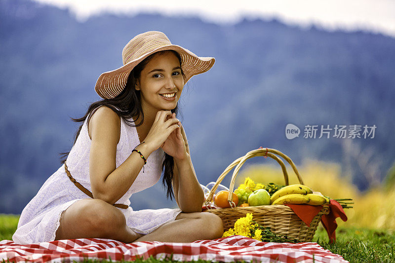 快乐的年轻女子准备野餐午餐坐在草地上