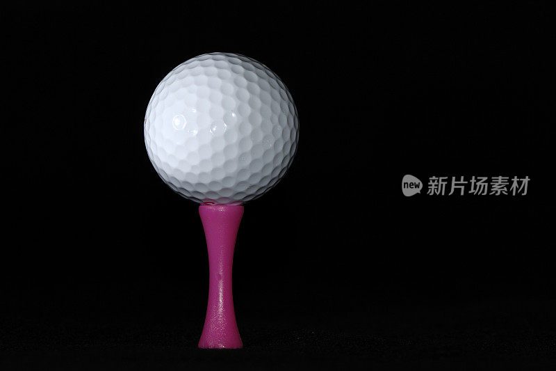粉红色球座上黑色背景的高尔夫球