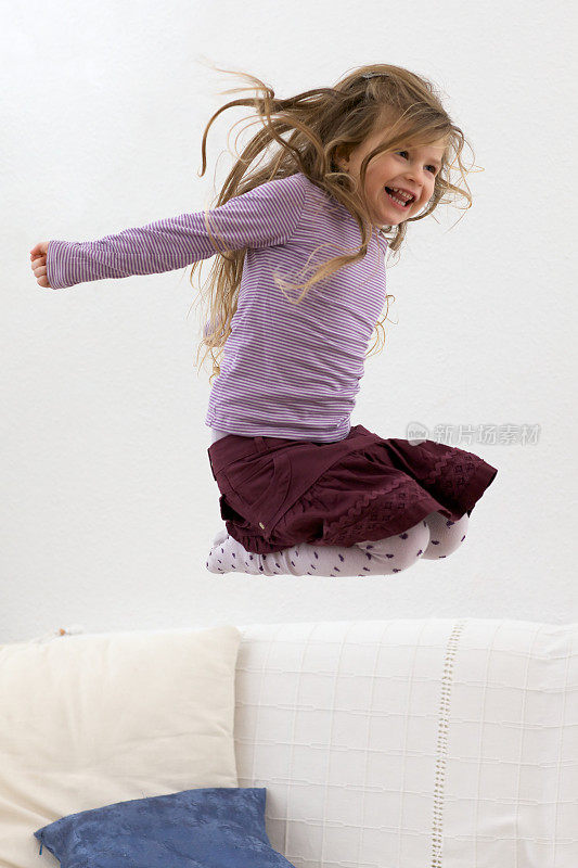 可爱的金发女孩在沙发上跳得很高