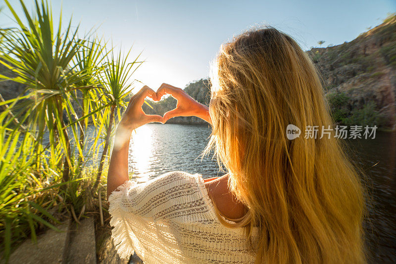 湖边的一个年轻女子做了一个心形的手指架