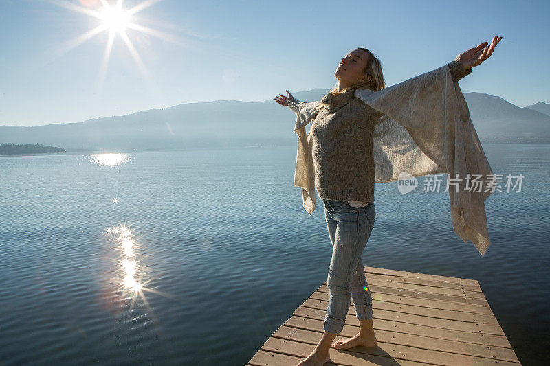 年轻女子在湖边码头上放松，双臂伸展