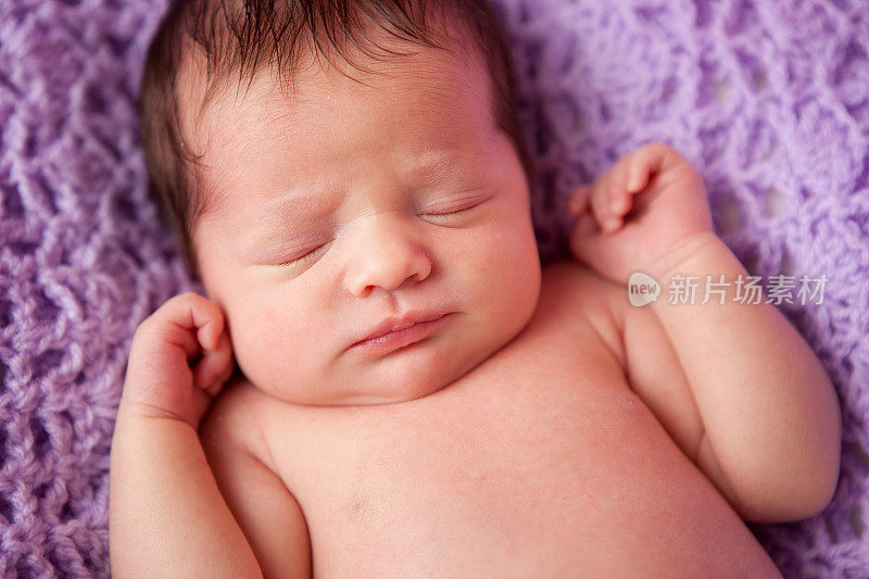 刚出生的女婴安静地睡在紫色的毯子上