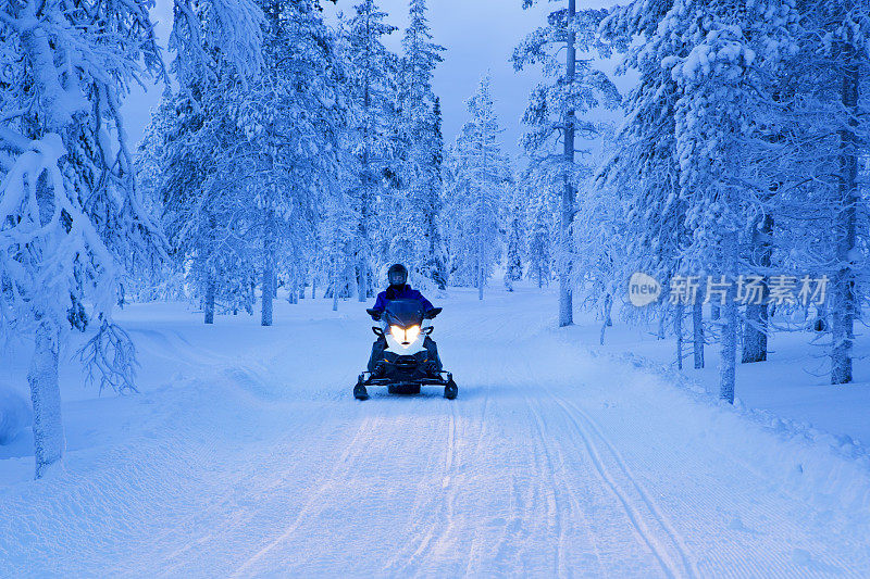 黄昏时分，芬兰拉普兰雪地摩托穿越冰冻的森林