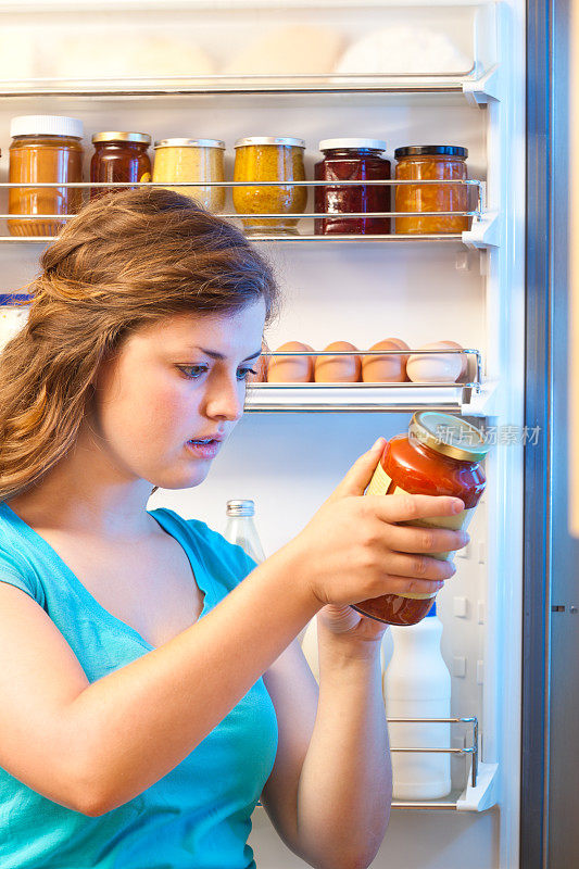 女人阅读食品标签，打开冰箱门研究成分