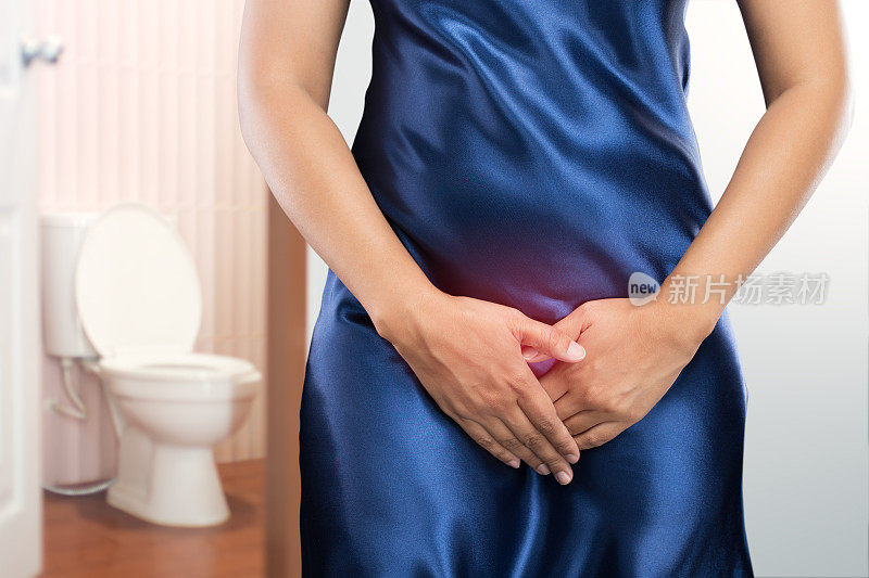 有前列腺问题的女人站在抽水马桶前。女士用手托着她的胯部，想小便的人有尿失禁的概念