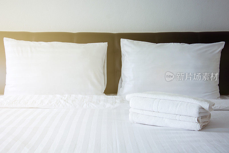 卧室床上白色枕头、白色毯子、白色毛巾，左侧上方有灯光