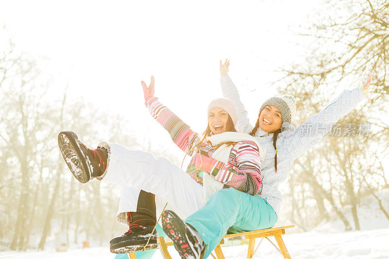 两个年轻女子在雪橇上举起双手