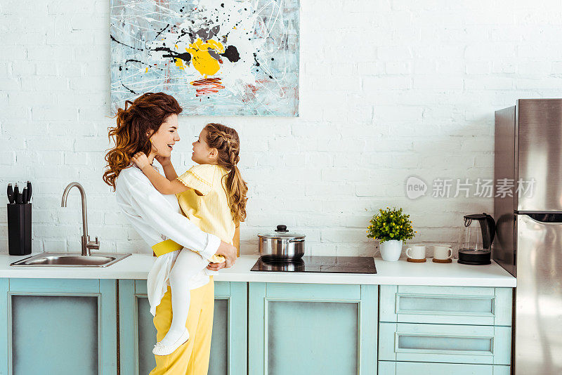 快乐的母亲抱着兴奋的女儿在厨房的侧面