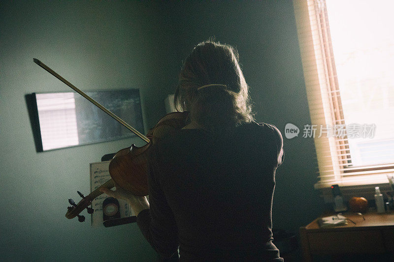 一位女小提琴家在家排练古典音乐作品的后视图