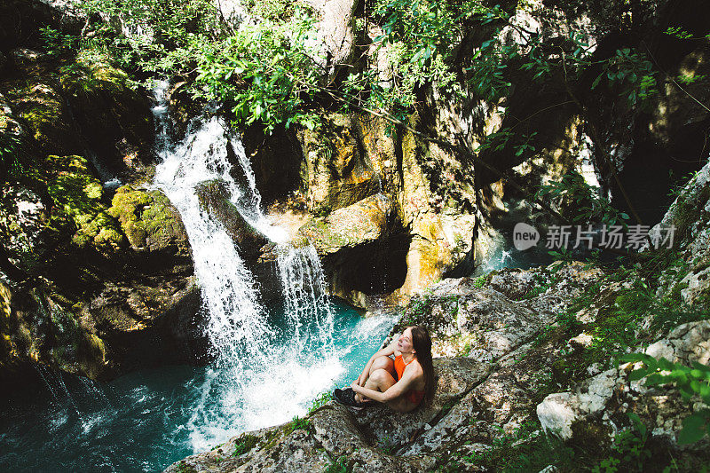 徒步旅行后，穿着泳衣的女人躺在瀑布附近的岩石上