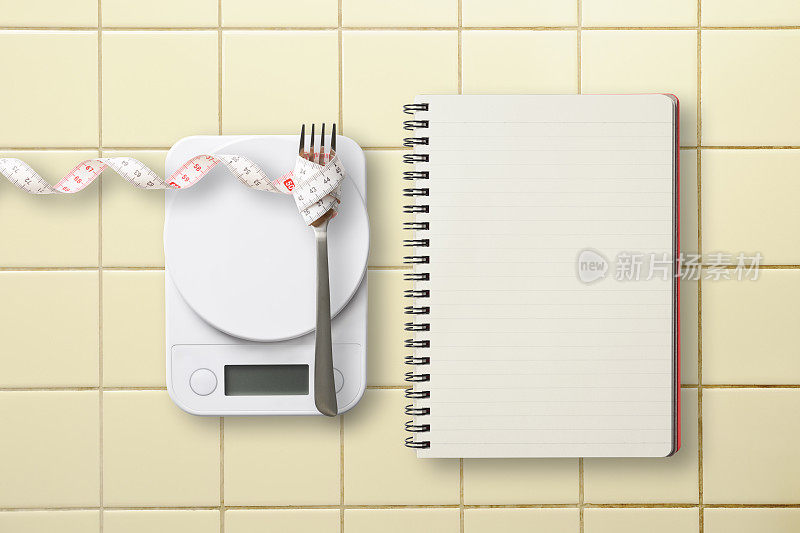 厨房数字食物秤和卷尺与空白食谱螺旋笔记本厨房瓷砖。