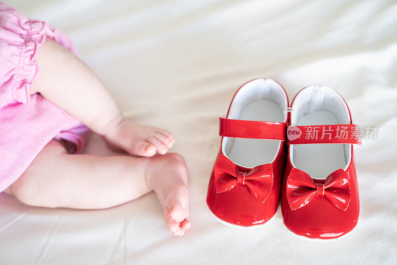 婴儿脚和红色的第一双鞋在床上的近距离照片