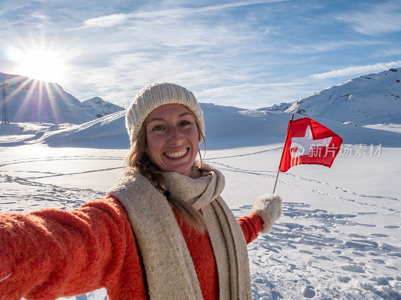 一名女子在瑞士阿尔卑斯山白雪皑皑的山上与瑞士国旗自拍