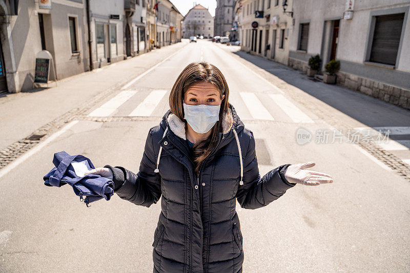 在病毒爆发封锁期间，一名戴口罩的成年妇女站在空城的道路中间，震惊地盯着摄像机――库存照片