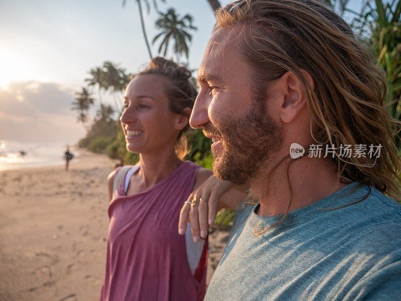 年轻夫妇在日落的热带海滩上拍手机自拍