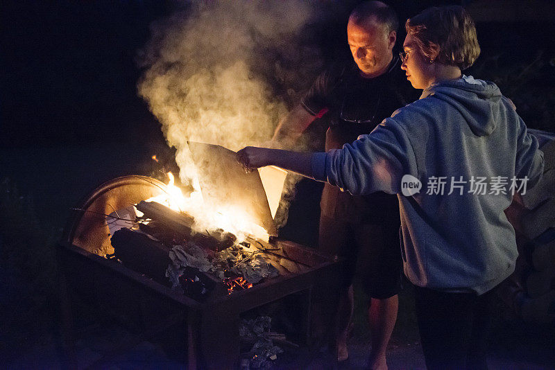 千禧一代的女人和高级男子在晚上在户外生火。