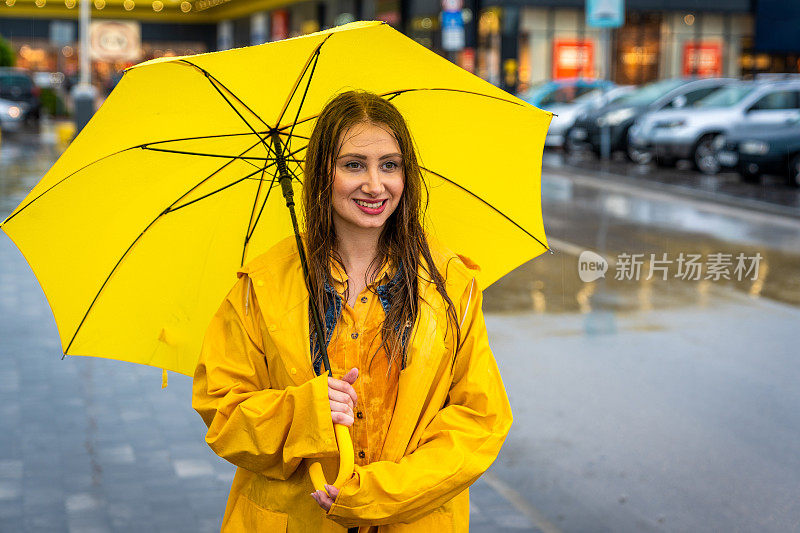 年轻女子拿着黄伞站在雨中。