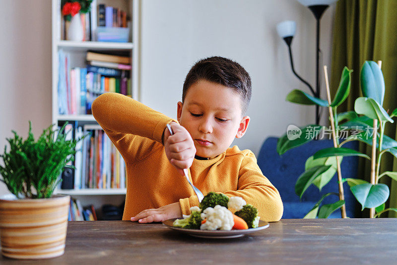 孩子对不得不吃蔬菜很不高兴。他的盘子里有许多蔬菜。他讨厌蔬菜。