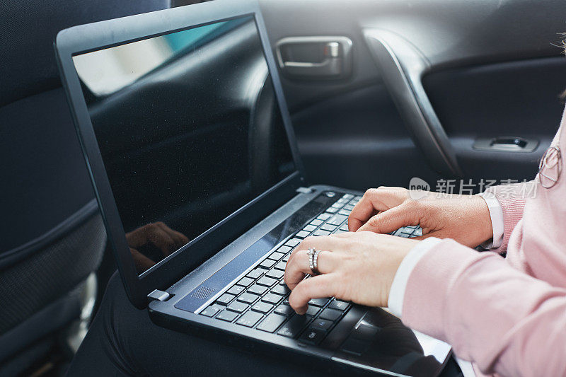 在一辆豪华轿车的后座上用笔记本电脑打字的女人