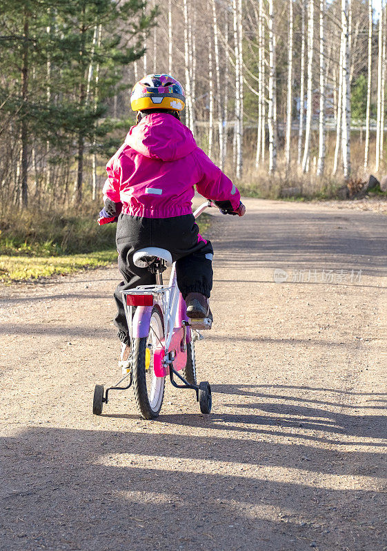 一个5岁的白人女孩，在乡下骑自行车。后视图。晴朗的秋日。