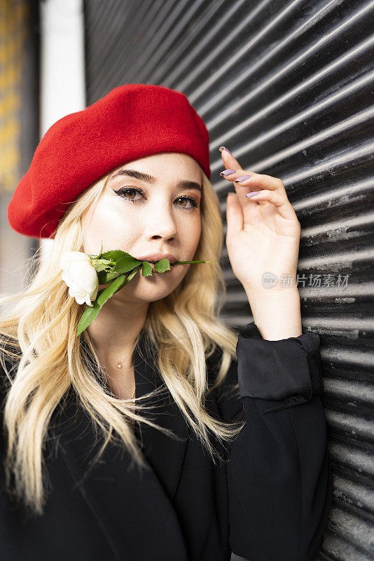 户外近距离肖像年轻美丽的金发女人。戴着红色贝雷帽的金发女人拿着白玫瑰