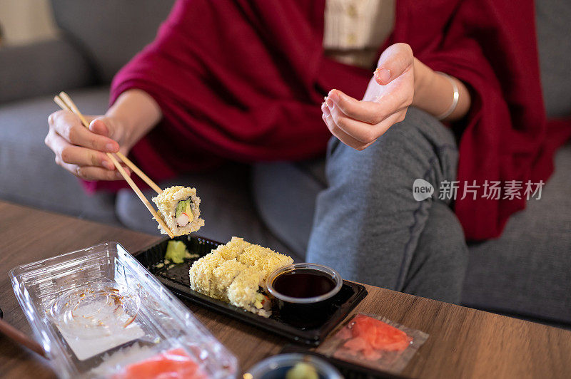 女人在家里吃着带酱的塑料包装的外卖或外卖寿司卷