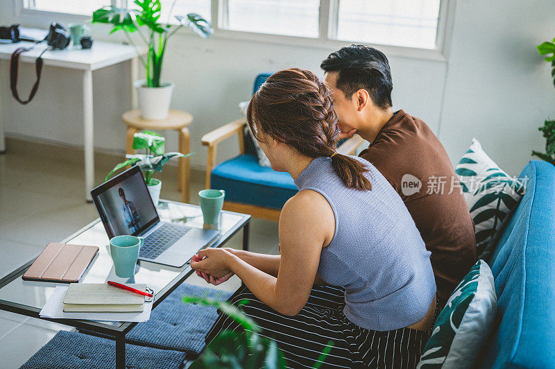 快乐的亚洲年轻夫妇使用笔记本电脑一起在客厅视频聊天