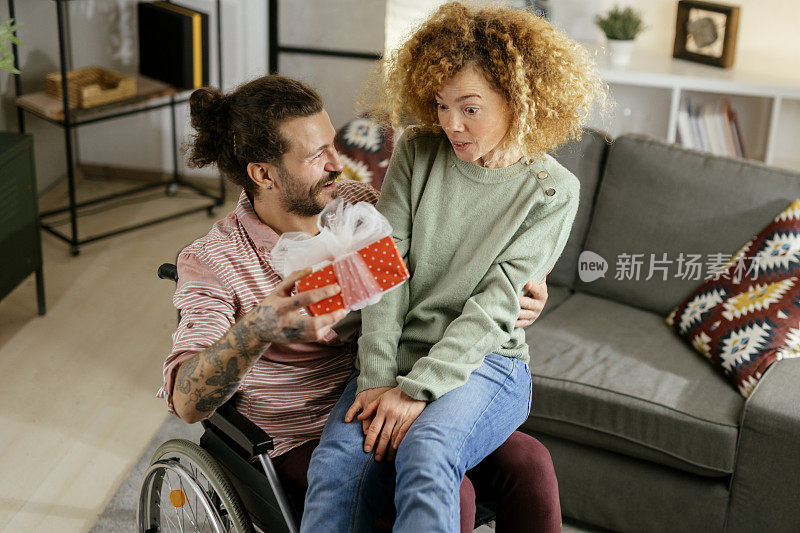 坐在轮椅上的年轻人在家里用礼物给他的女朋友惊喜照片