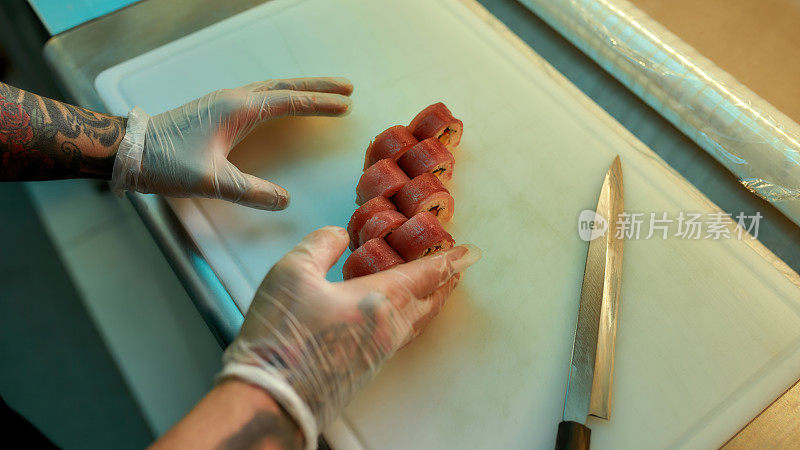 厨师切金枪鱼寿司的手的特写镜头，同时准备在一个商业厨房的板上卷