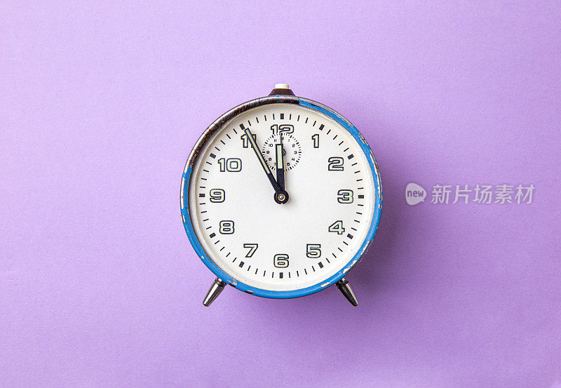 旧的复古模拟闹钟在蓝色上的紫色背景。钟从5分钟到12点开始。