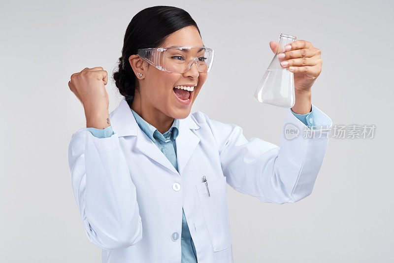 一名迷人的年轻女科学家在研究一个装满液体的烧杯时欢呼的镜头，背景是灰色