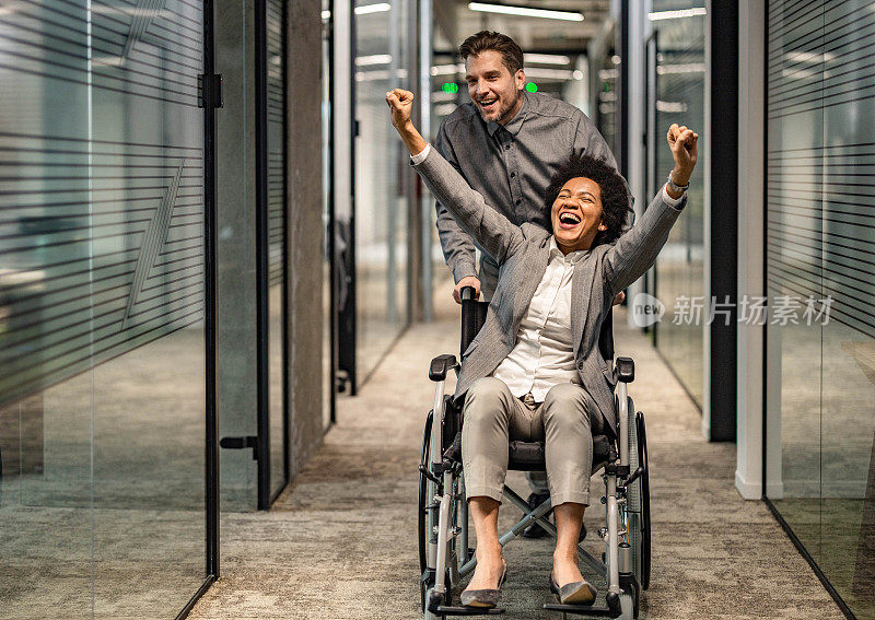坐轮椅的黑人女商人和同事在走廊里玩得很开心。