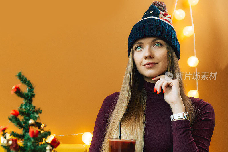 拿着热葡萄酒，戴着美国帽子的女人。圣诞画像用酒，人是喝烈性酒。在桌子上的圣诞树。新年摄影。
