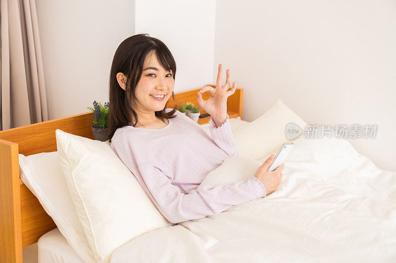 漂亮的亚洲女人在床上用智能手机