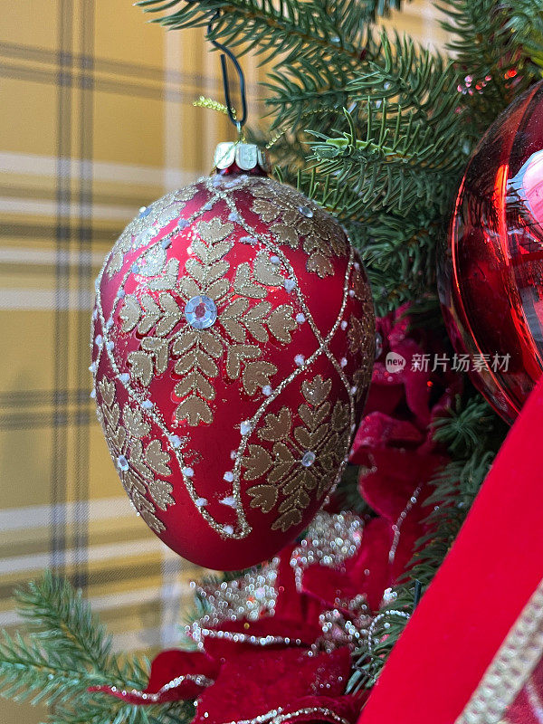 形象的个人，红色的蛋形装饰品装饰着闪光和宝石挂在人造圣诞树的树枝上，云杉针，模糊的白色神仙灯的背景